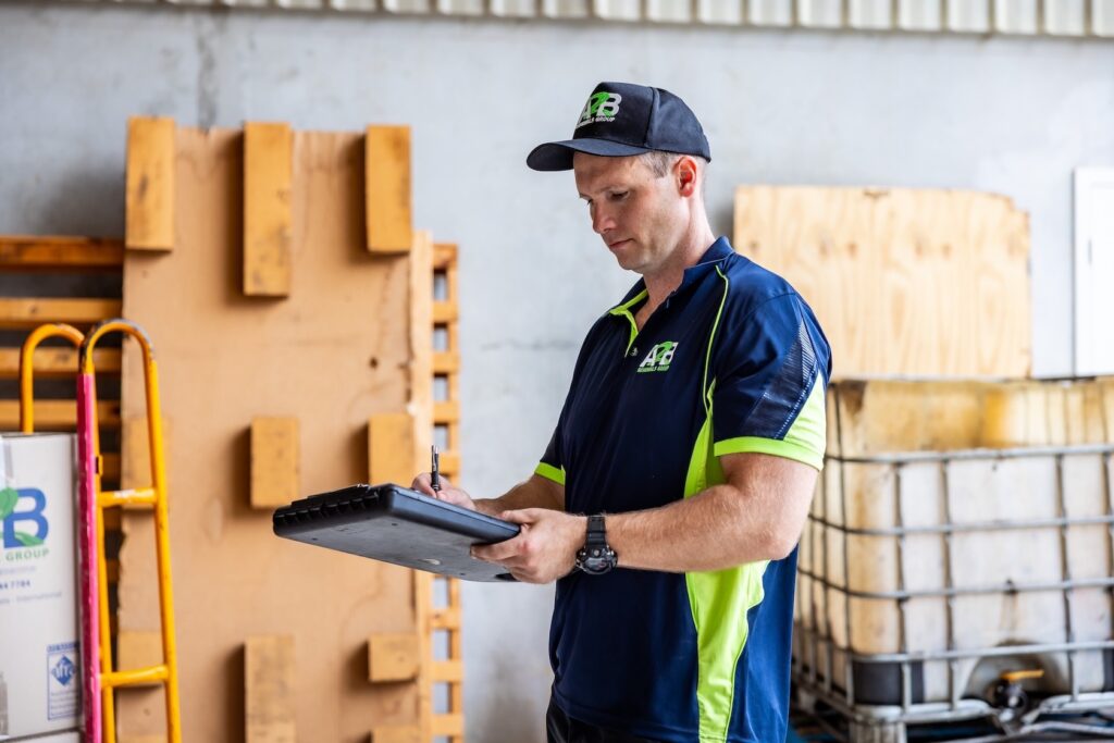 A2B Removals team member in uniform, checking an interstate moving plan on a clipboard inside a storage warehouse